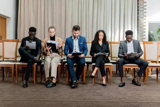 group of people from different races sat down on chairs against a wall, symbolising no bias in recruitment